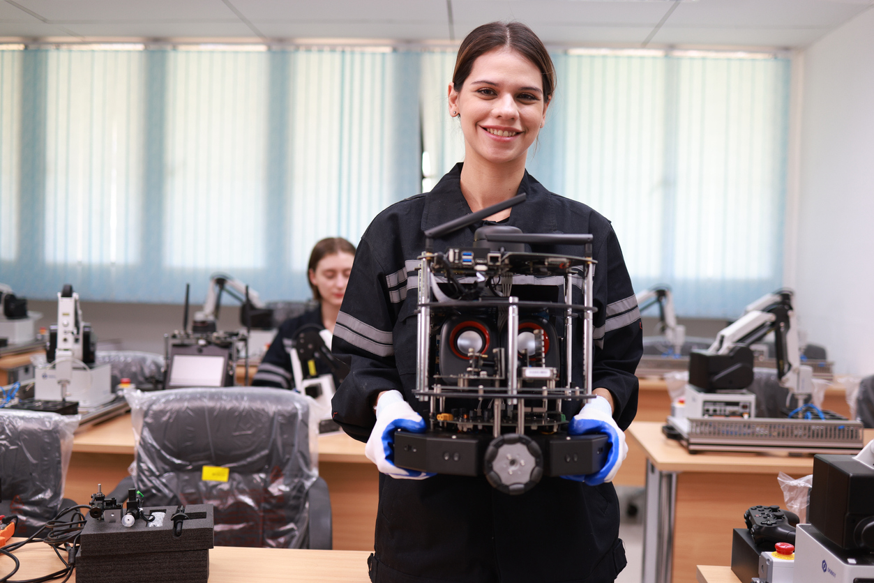 Woman holding robot in a classroom setting.