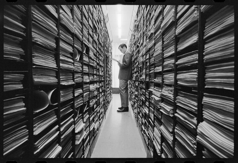 Man reading in archive room with shelves.