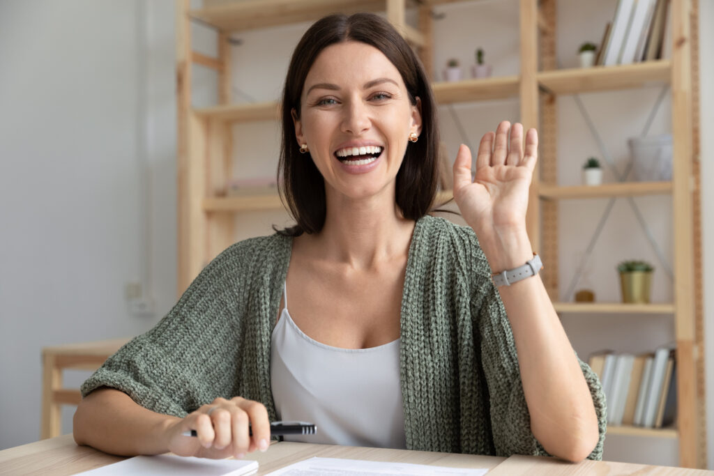 Smiling woman waving in a home office.