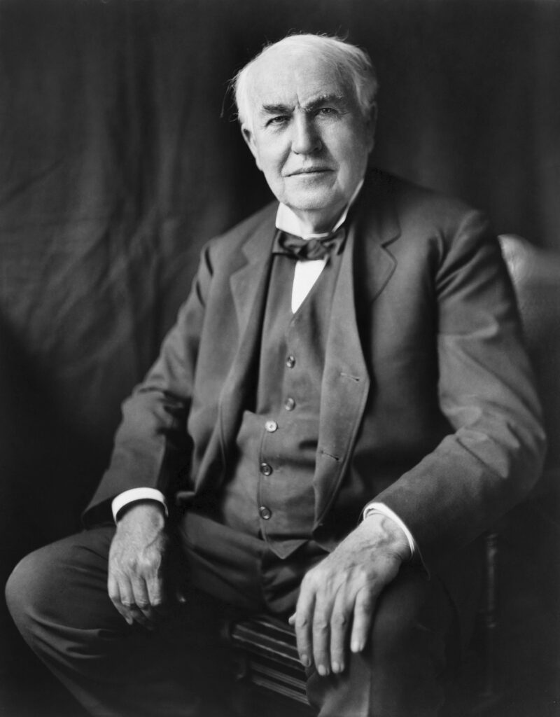 Elderly man in suit sitting, black background.